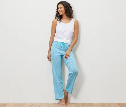 Duvara yaslanmış bir kadın beyaz bir atlet ve mavi çizgili bir pijama altı giyiyor.