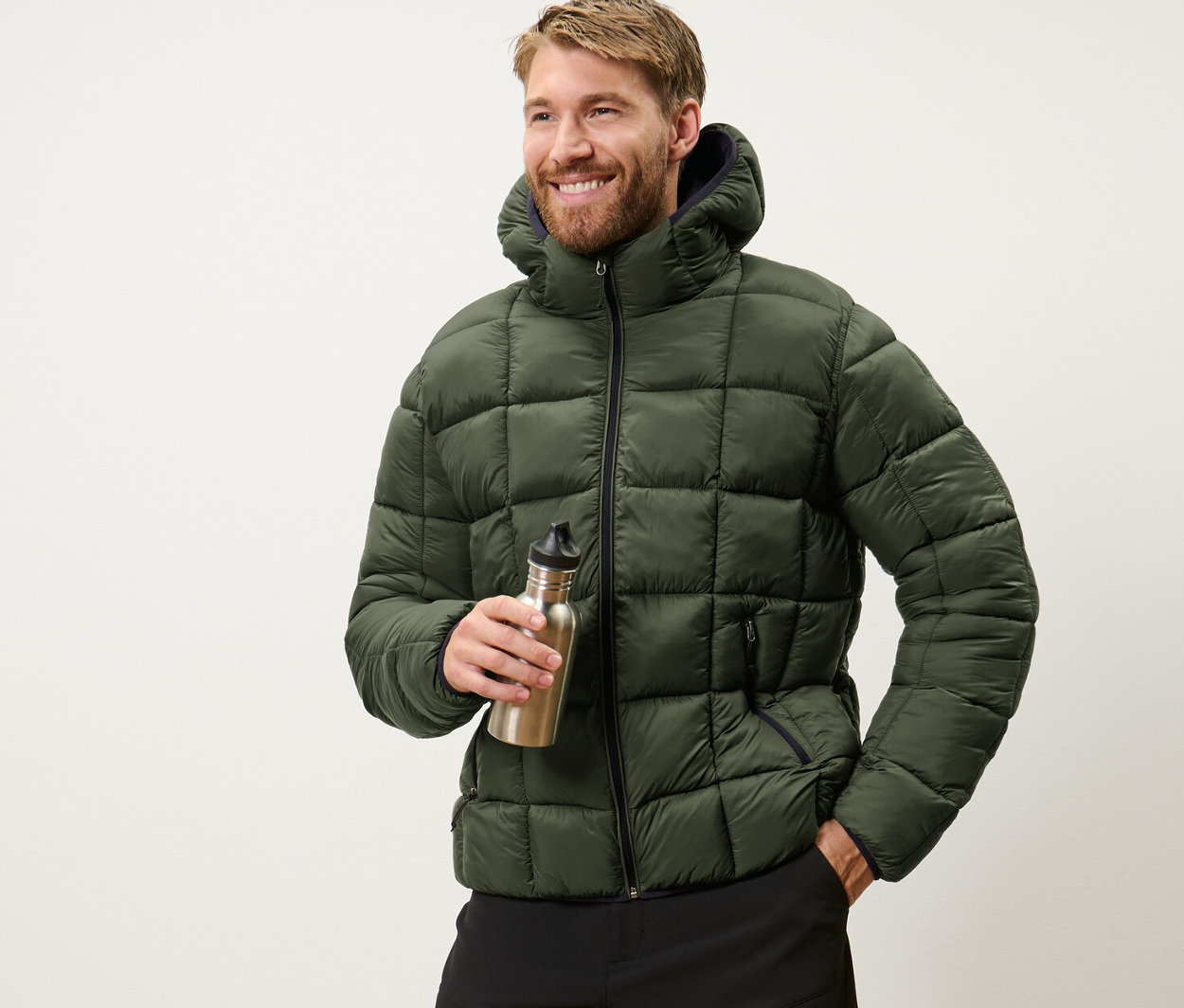 Adam bir su şişesi tutuyor ve haki kapitone mont giyiyor.