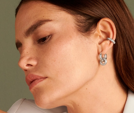 Kadın oturuyor ve Kıkırdak Küpesi Parlak Donut, Yüzük Parlak Donut, Halka Küpe Sparkle Donut ve Kolye Parlak Donut takıyor.