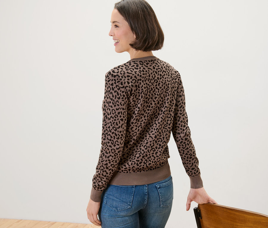 Kot pantolonlu ve baskılı ince örgü hırkalı bir kadın sandalyenin yanında poz veriyor.