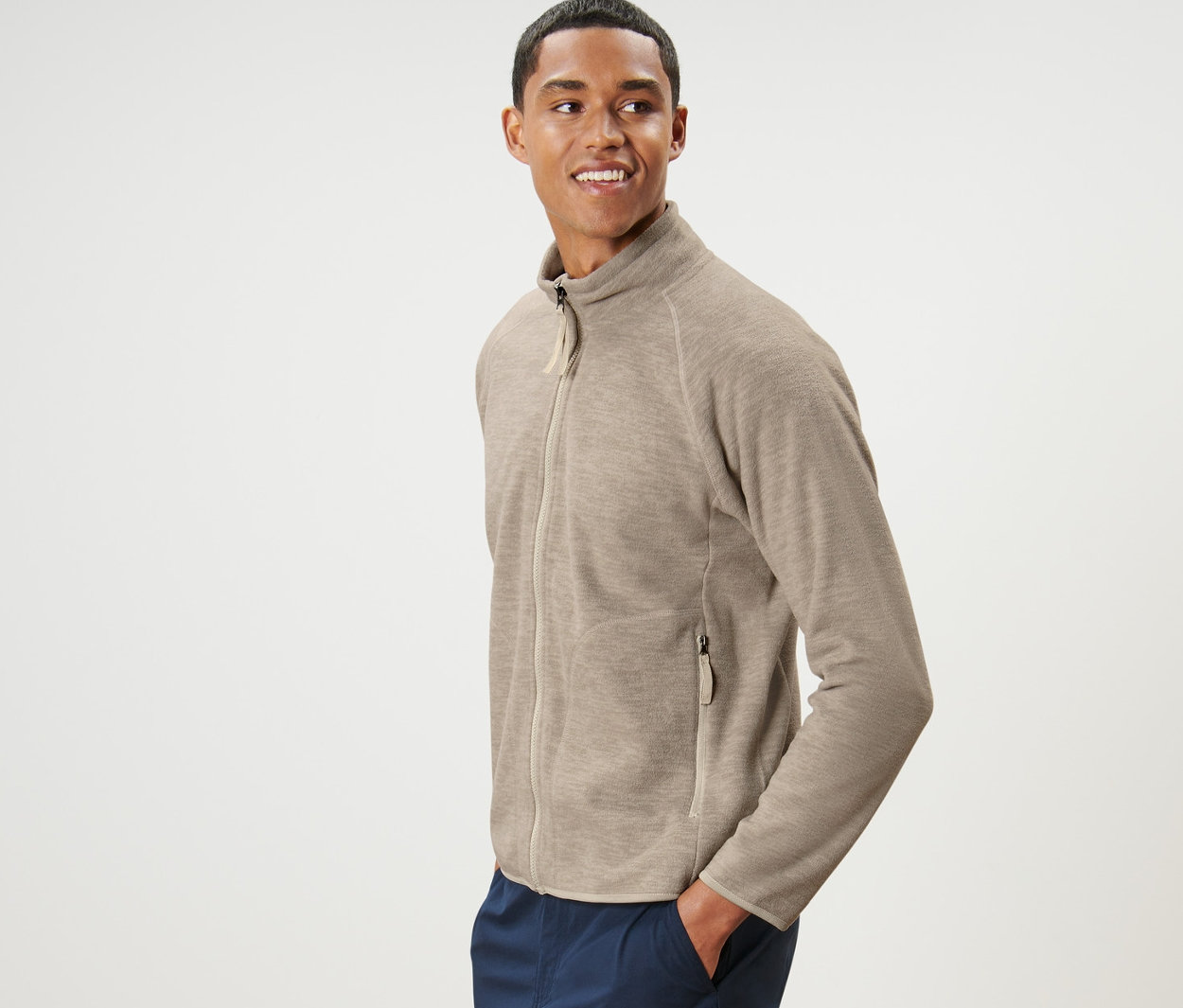 Adam bej rengi polar ceket ve lacivert pantolonla poz veriyor.