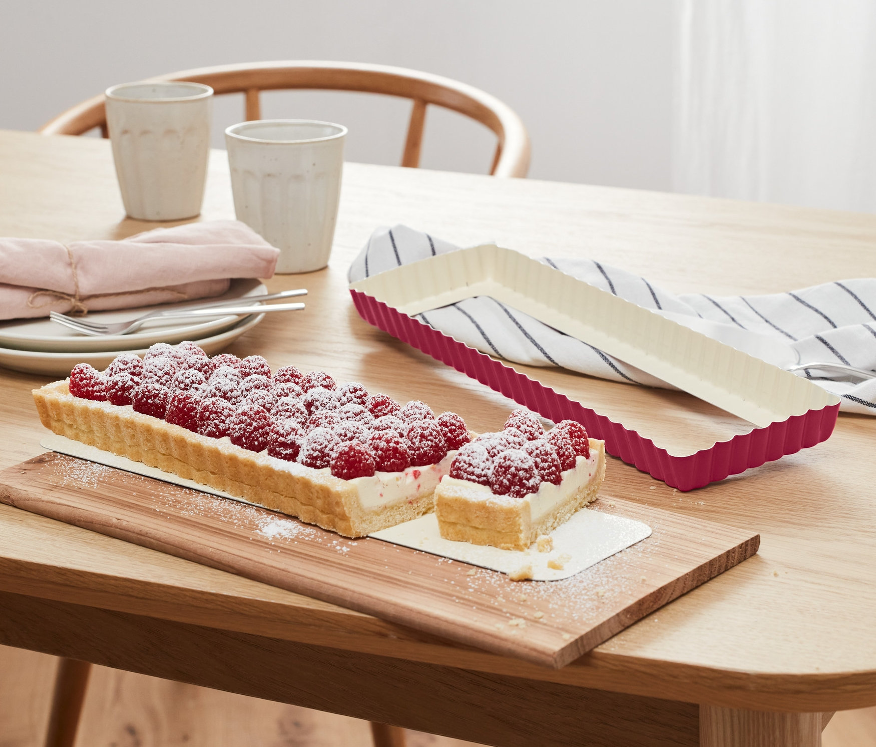 Ahşap bir masa üzerinde bir tart kalıbı ve kesilmiş bir ahududulu tart bulunmaktadır.