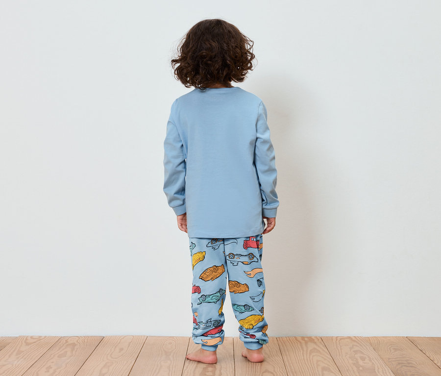 Sırtı kameraya dönük bir çocuk, üzerinde küçük araba baskısı olan mavi bir pijama giyiyor.