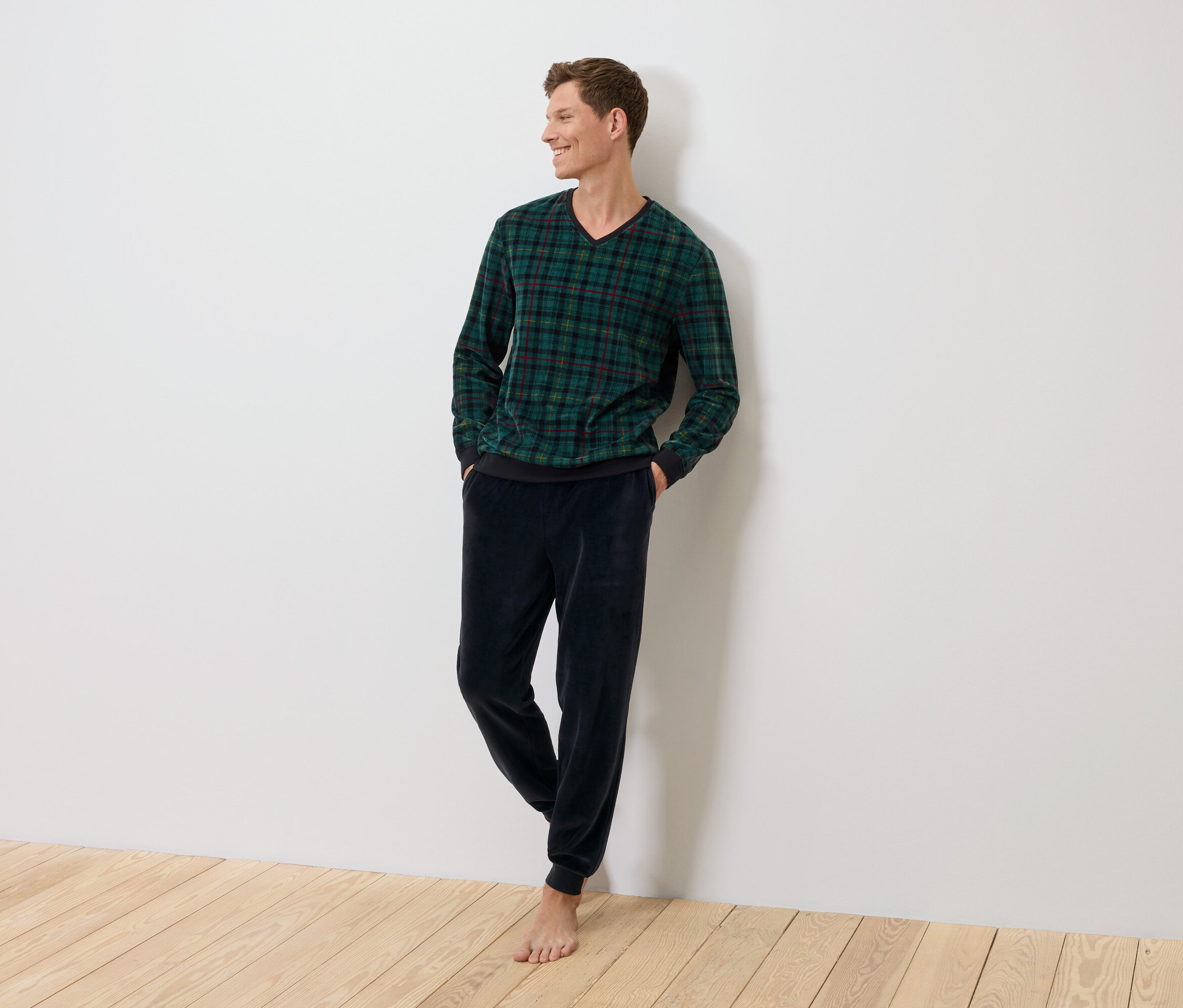 Bir adam duvara yaslanmış, yeşil ekose bir kazak ve koyu mavi kadife pantolon giyiyor.