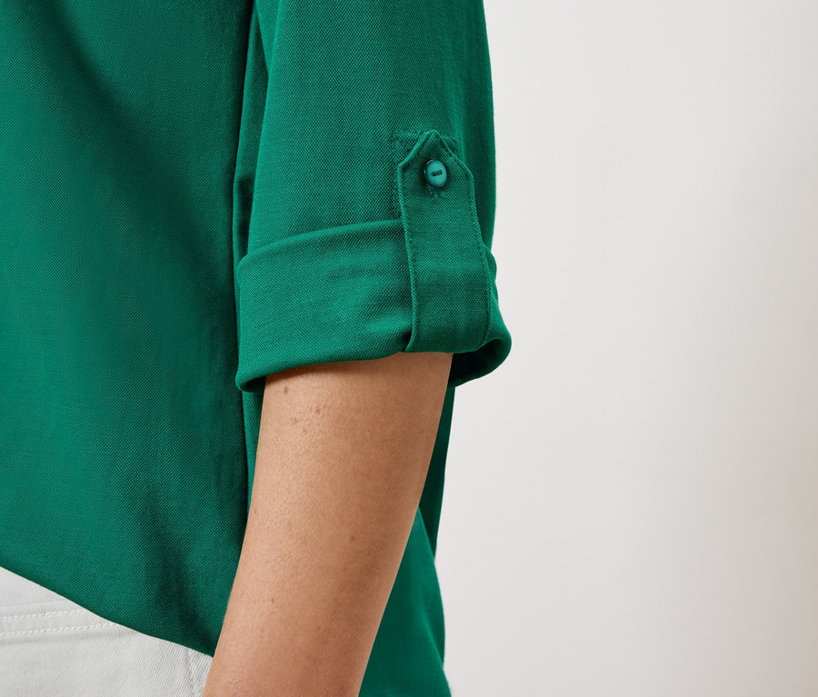 Düğmeyle tutturulmuş, yukarı sıvanmış kollu, kadınlara ait yeşil bir gömleğin yakın çekim detayı.