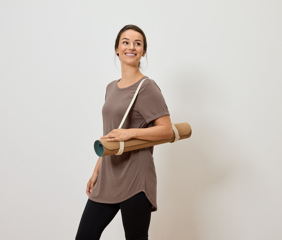 Gülümseyen bir kadın omzunda yoga matı taşıyor.