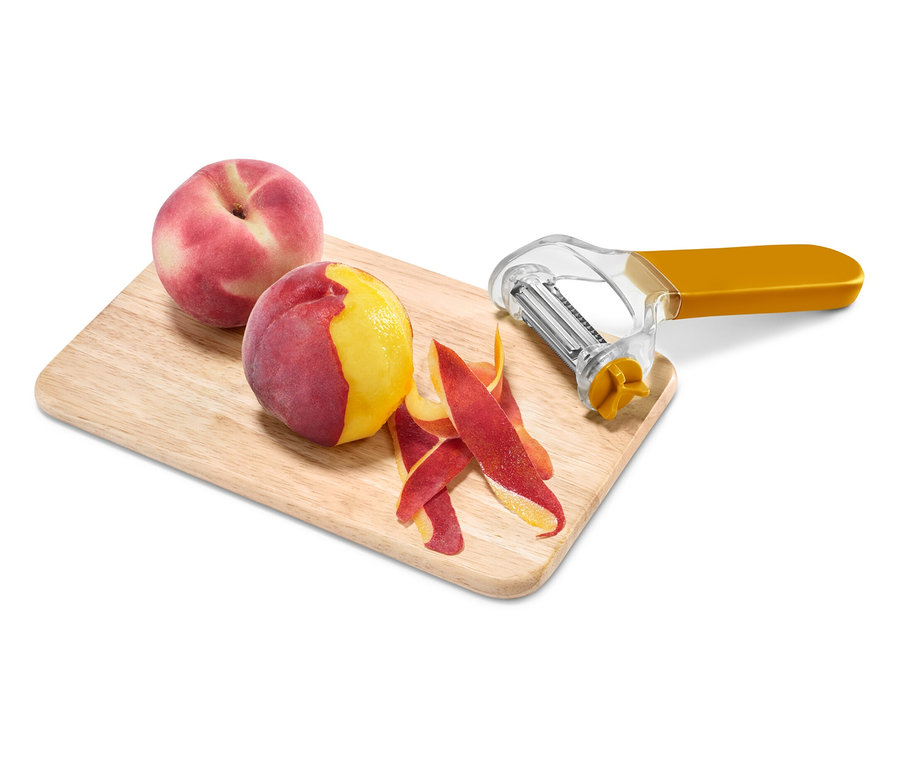 İki şeftali, biri ahşap bir tahta üzerinde sarı bir soyucu ile soyulmuş.