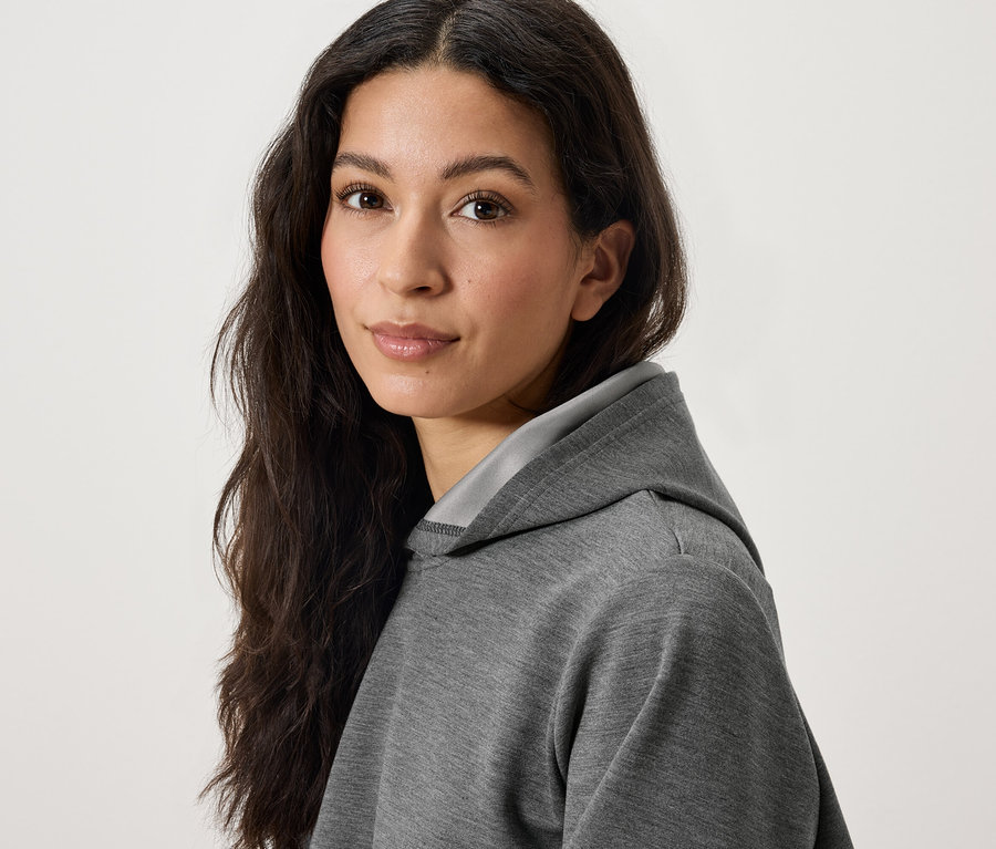 Uzun, koyu renk saçlı, gri kapüşonlu sweatshirt giyen bir kadının portresi.
