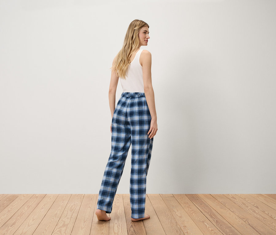 Beyaz atlet ve mavi kareli pantolonlu kadın ahşap zeminde duruyor.