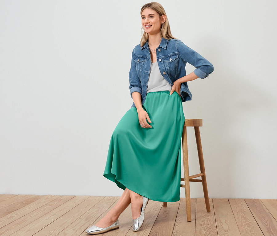 Kadın taburede oturuyor, üzerinde Kot Ceket, Satén Etek ve Beyaz Dokulu Tişört var.