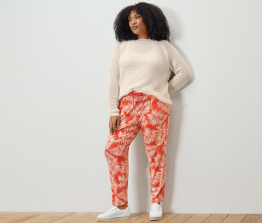 Bir kadın, pointelle örgü kazak ve baskılı jarse pantolon giyerek poz veriyor.