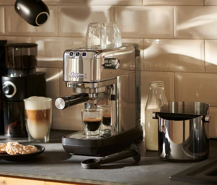 Tezgâhta duran gümüş renkli »Lapressa« Portafiltre Makinesi, bir bardağa espresso hazırlıyor.