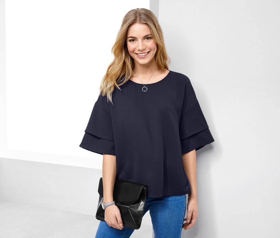 Kadın lacivert mavi dokuma tişört ve mavi kot pantolonla poz veriyor.