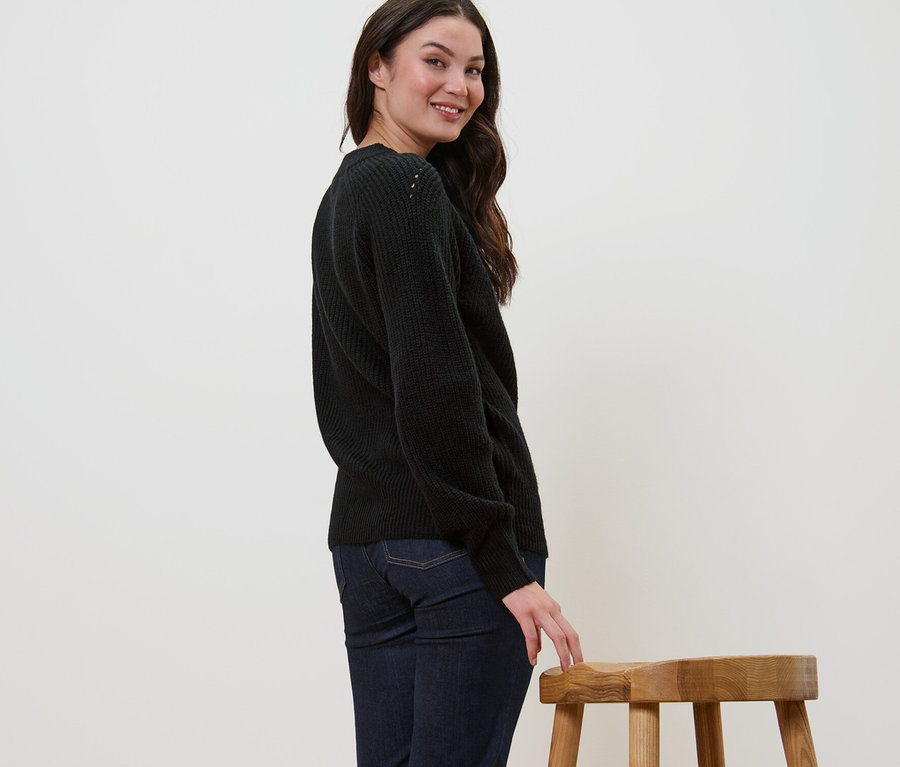 Kadın omzunun üzerinden gülümsüyor ve siyah örgü kazakla poz veriyor.