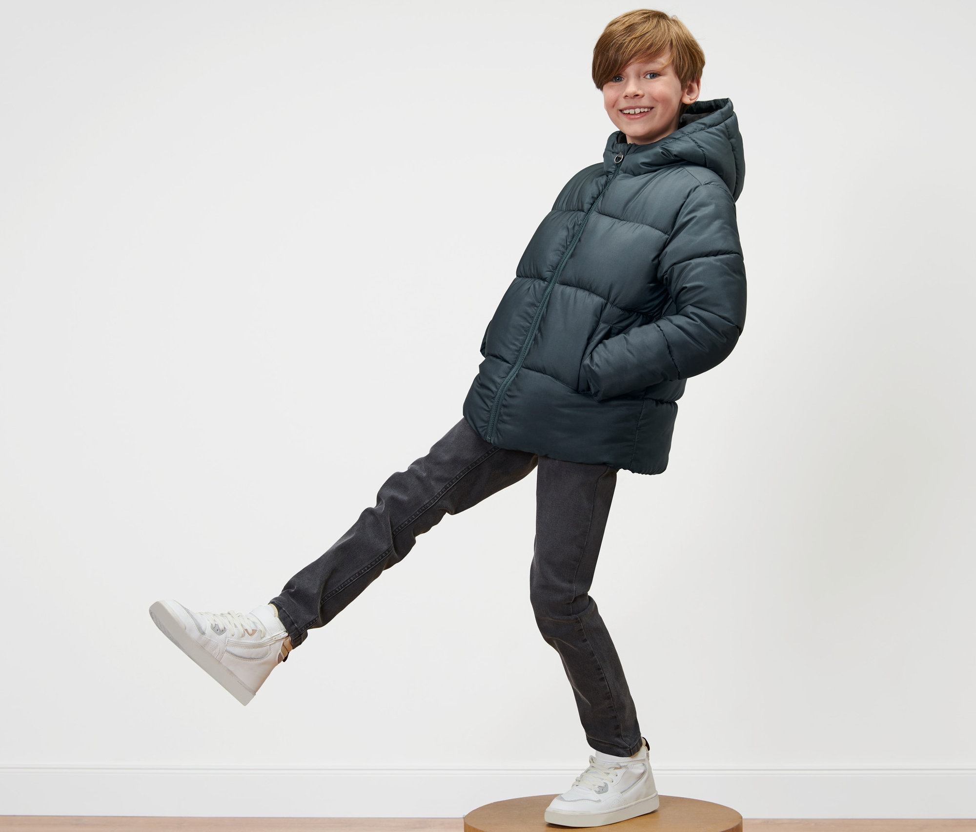 Çocuk, Çocuk Termal Mont ve spor ayakkabılarıyla ahşap bir kaide üzerinde poz veriyor.