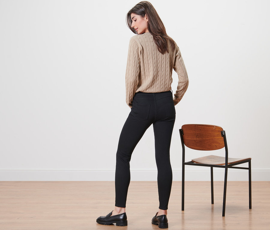 Bir kadın kameraya arkası dönük duruyor, bej bir kazak ve tayt pantolon giyiyor.