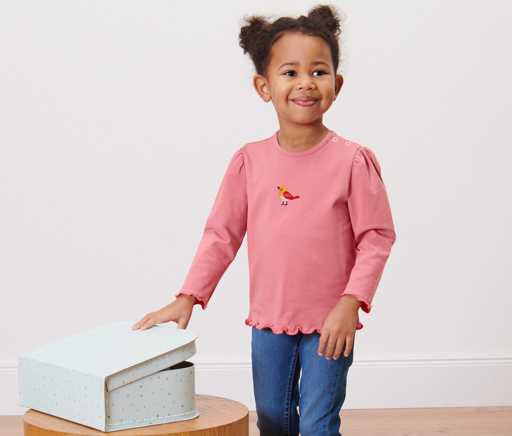 Pembe 2 Adet Çocuk Uzun Kollu Tişört giyen kız çocuğu, açık bir kutunun yanında duruyor.