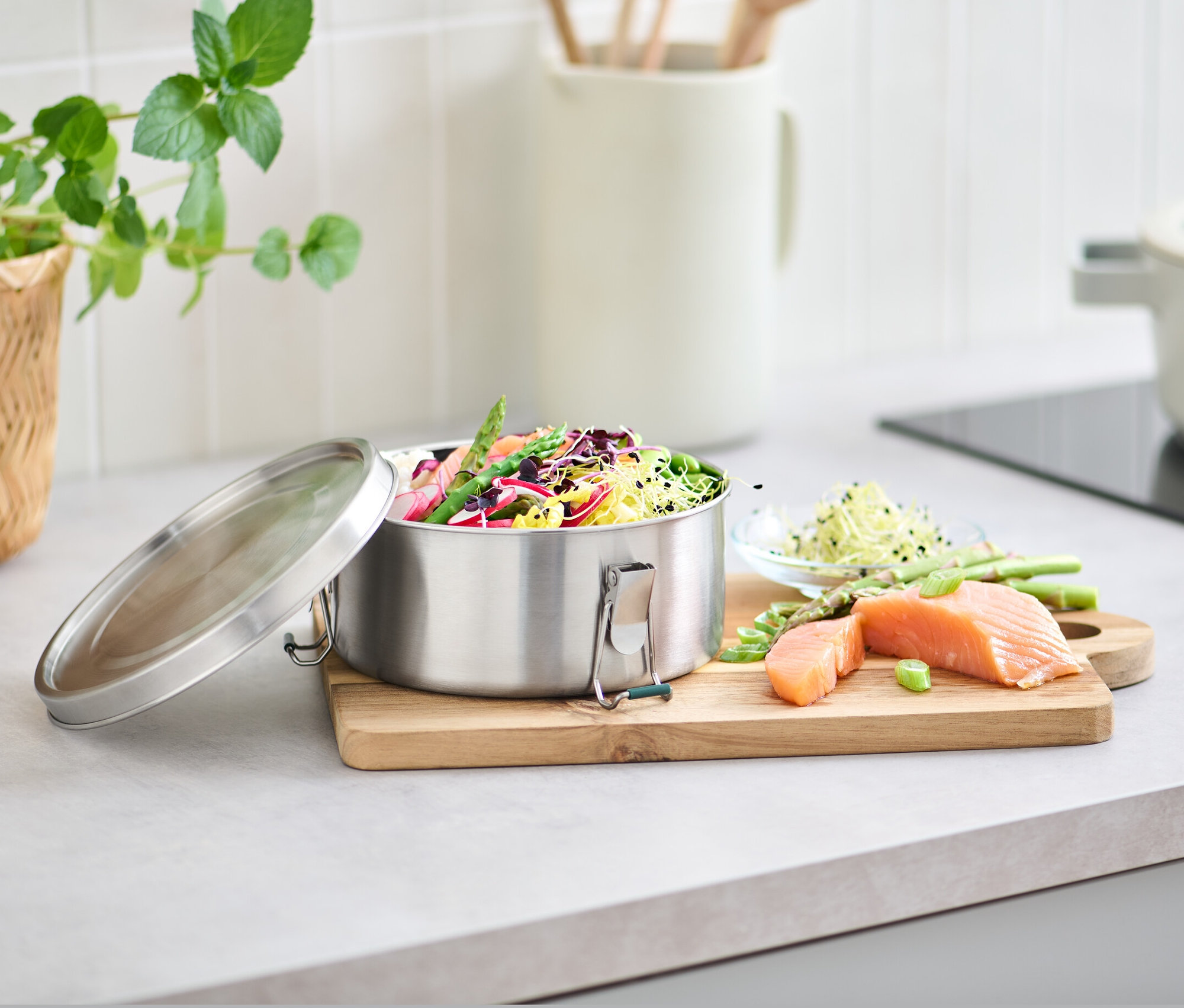 Sebze ve salata dolu paslanmaz çelik sefer tası, yanında kesme tahtası üzerinde somon ve kuşkonmaz.