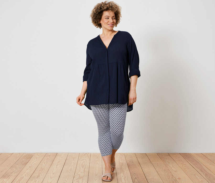 Bir kadın uzun bir bluz ve baskılı 3/4 tayt giyiyor.