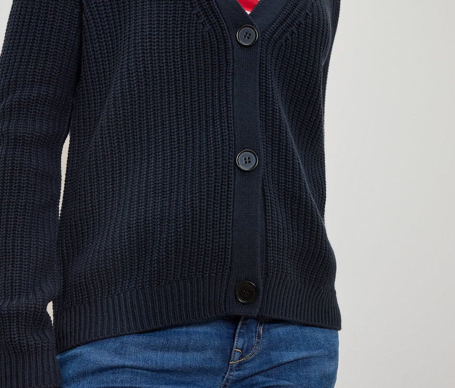 Düğmeli lacivert örgü hırka ve mavi kot pantolon giyen bir kişinin vücudu.