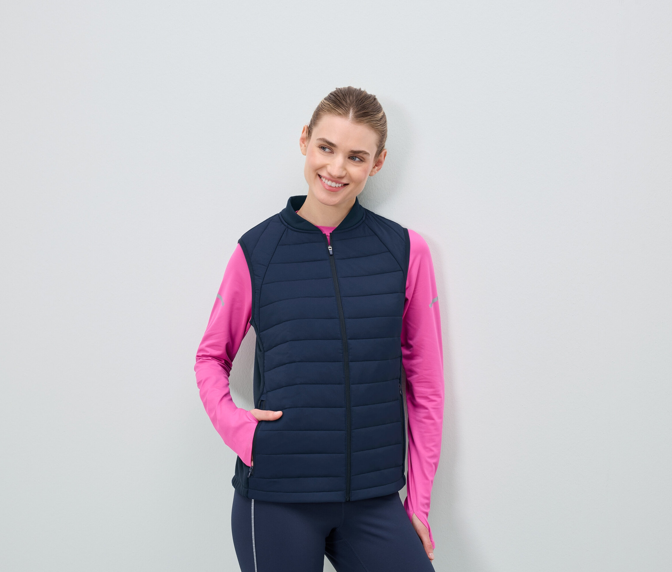 Koyu lacivert kapitone yelek ve pembe uzun kollu üst giyen kadın.