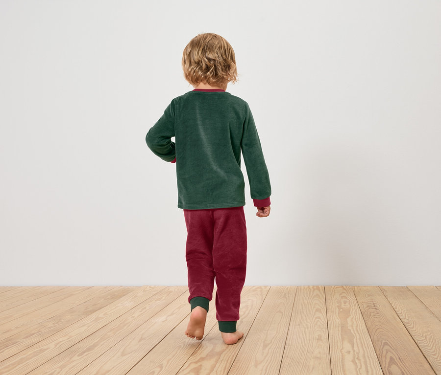 Yeşil pijamalık ve bordo pijamalı bir çocuk, ahşap zeminde yalın ayak yürüyor.