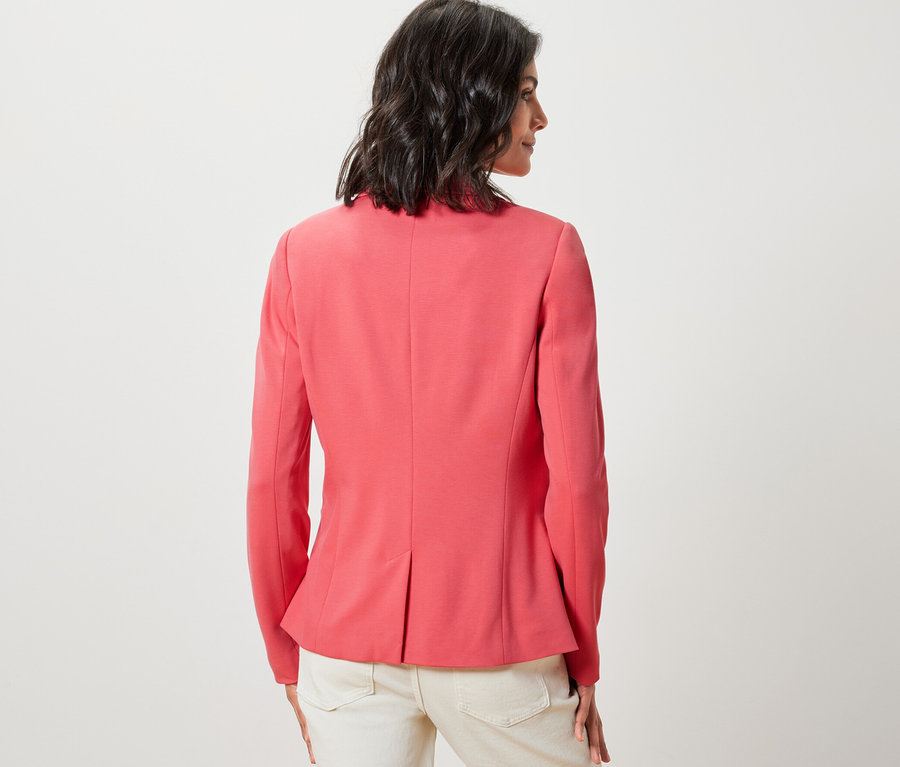 Kadın arkası dönük duruyor, mercan rengi Jersey Blazer Ceket ve açık renk pantolon giyiyor.
