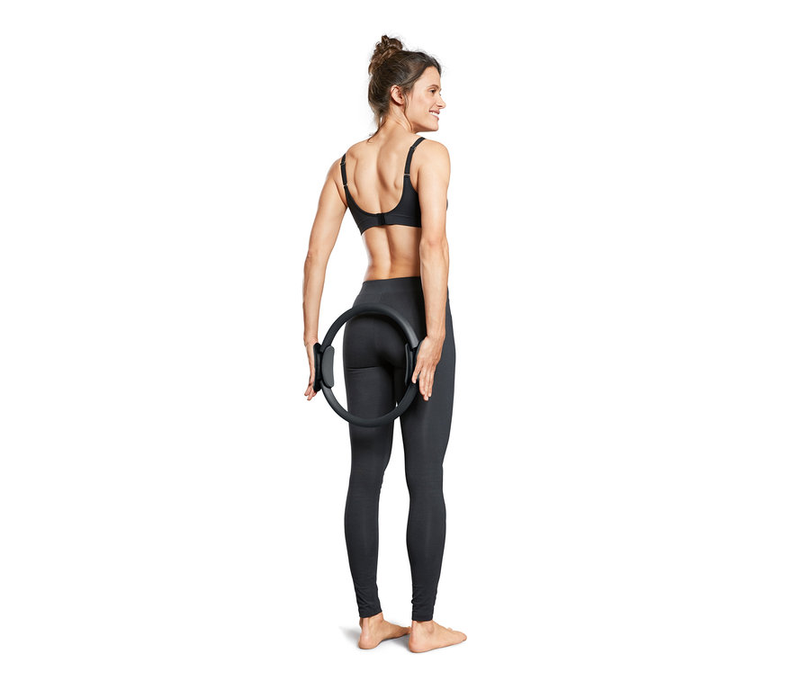 Kadın sırtının arkasında siyah bir Pilates Halkası tutuyor.