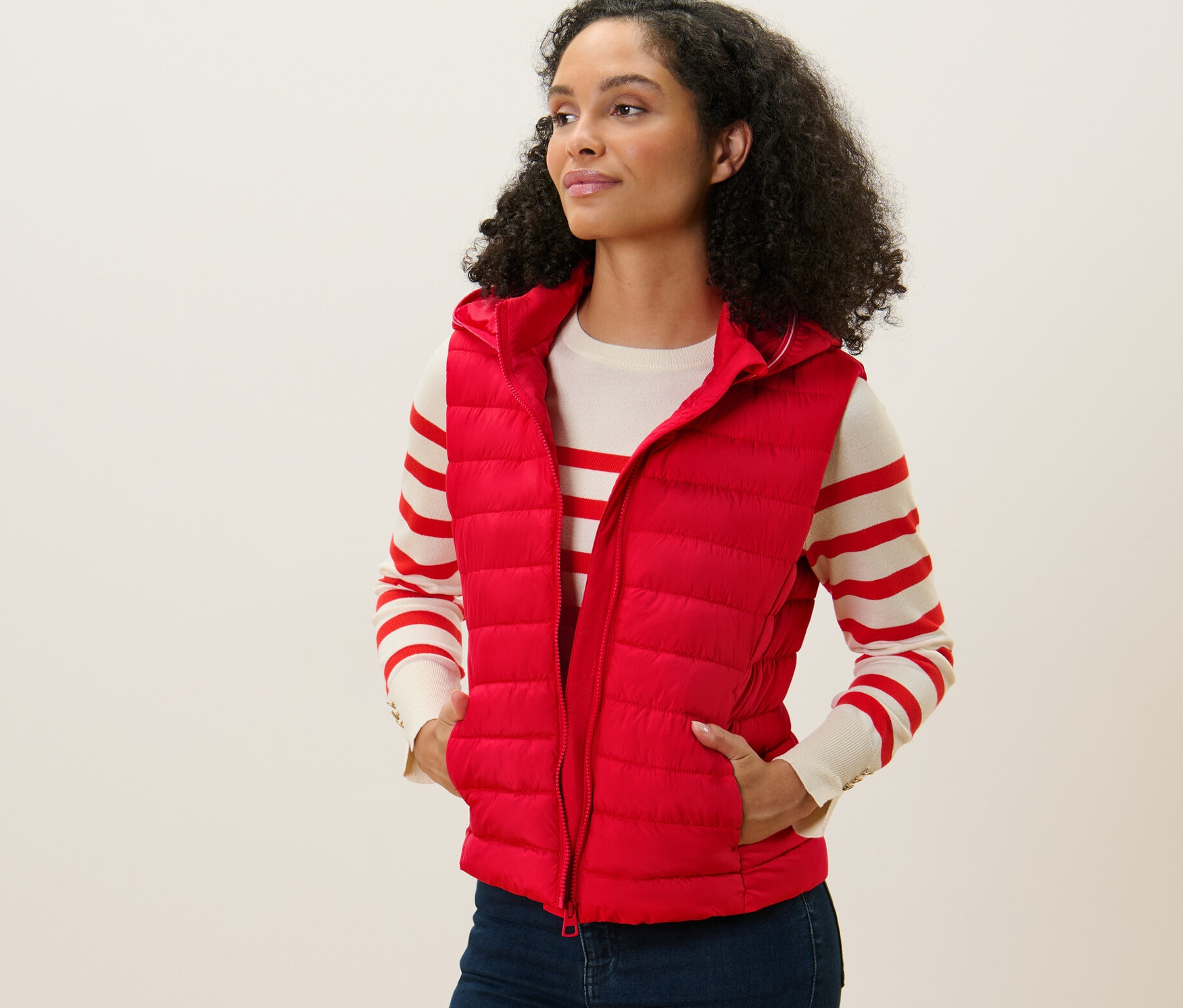 Kadın kırmızı kapüşonlu kapitone yelek giyiyor, ayakta duruyor ve sola bakıyor.