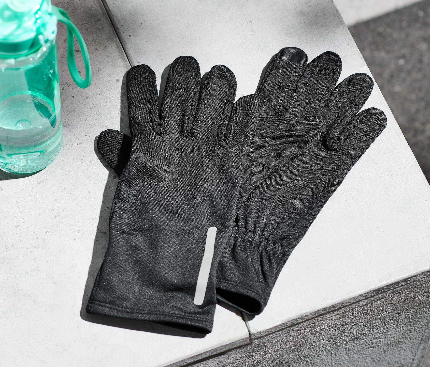 Beton bir yüzeyde bir çift koşu eldiveni ve bir su şişesi duruyor.