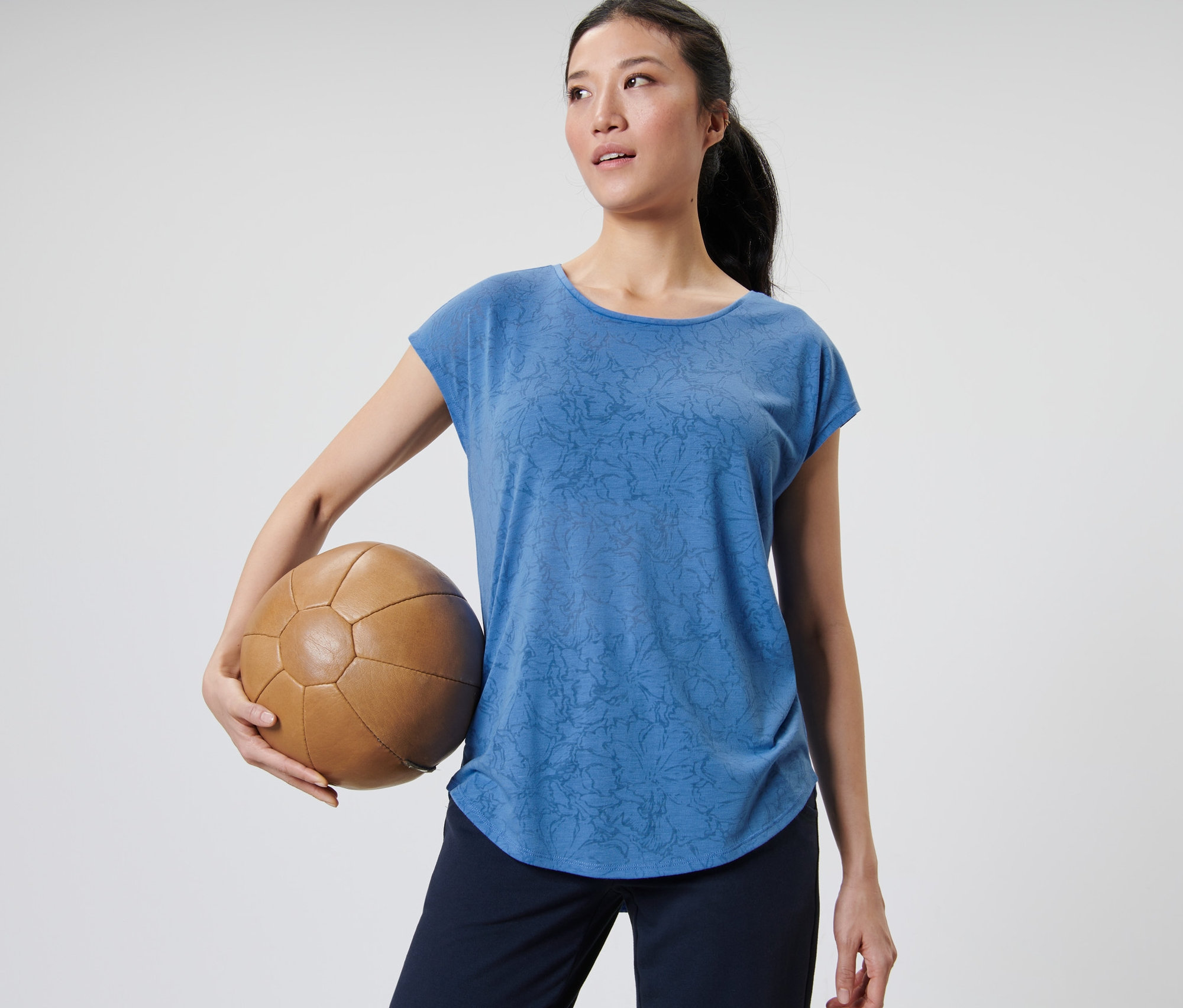 Kadın kahverengi deri bir top tutuyor ve mavi bir spor tişörtü giyiyor.