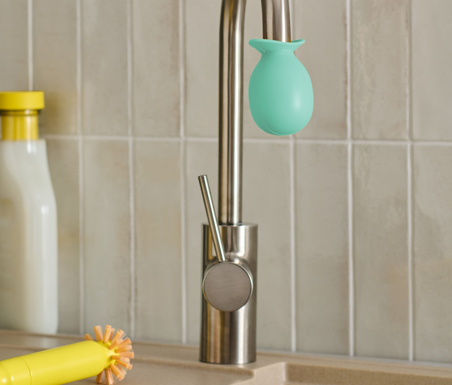 Bir musluğun üzerinde yeşil bir musluk kireç çözücü başlığı var. Yanında sarı bir fırça ve bez var.