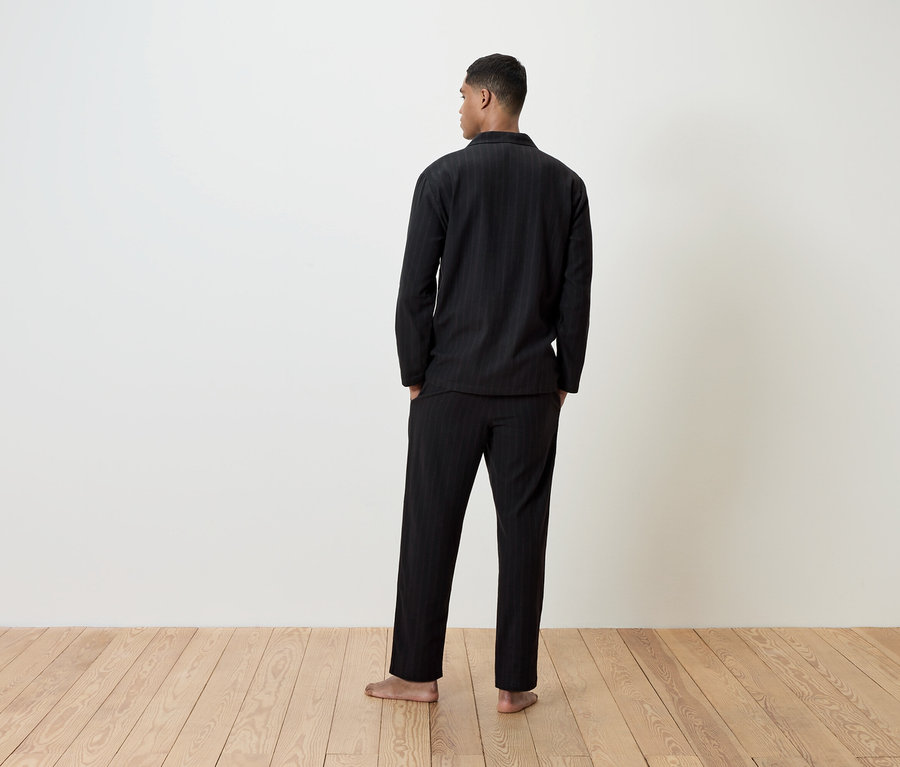 Siyah pijamalı bir adam kameraya arkası dönük duruyor.