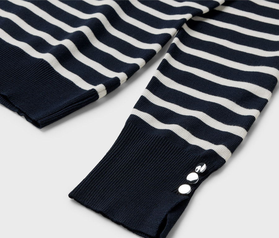 Manşetinde gümüş düğmeler bulunan, lacivert beyaz çizgili, uzun kollu bir kazağın yakın çekim detayı.