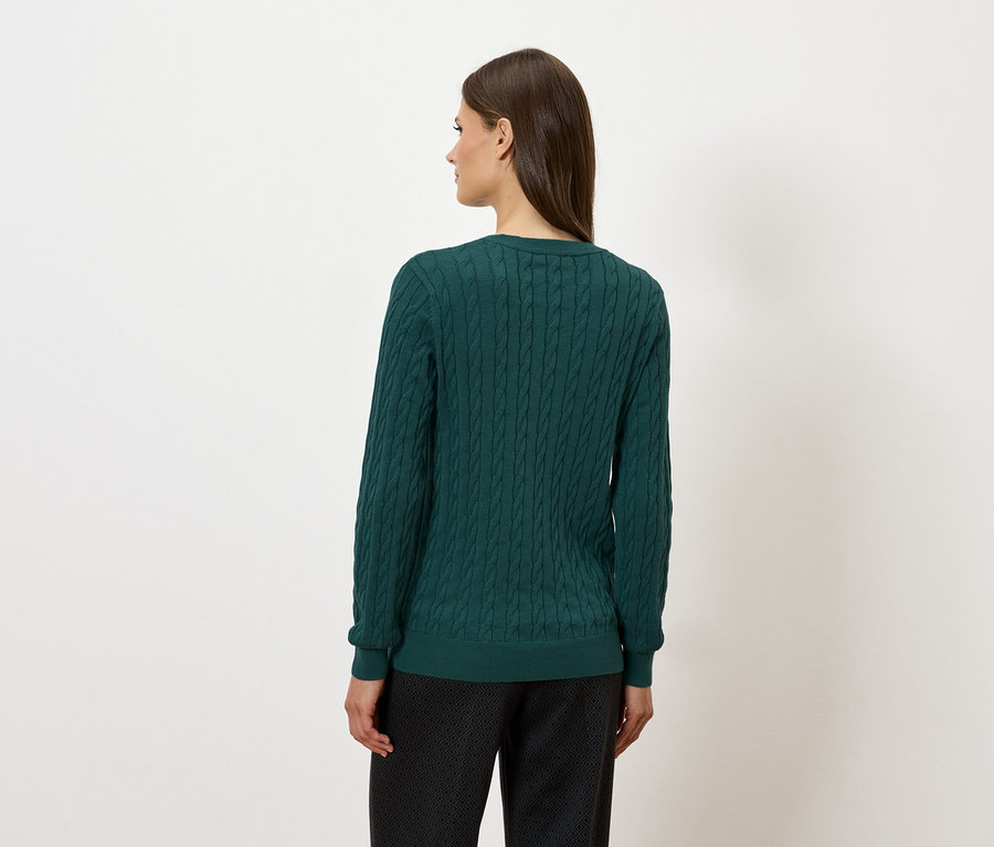 Arkadan görünen, yeşil bir kazak ve koyu renkli pantolon giyen bir kadın.