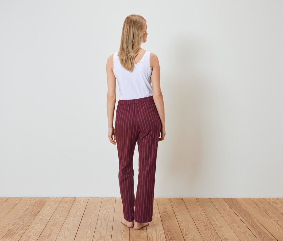 Kadın arkası dönük duruyor, beyaz bir atlet ve bordo çizgili pantolon giyiyor.