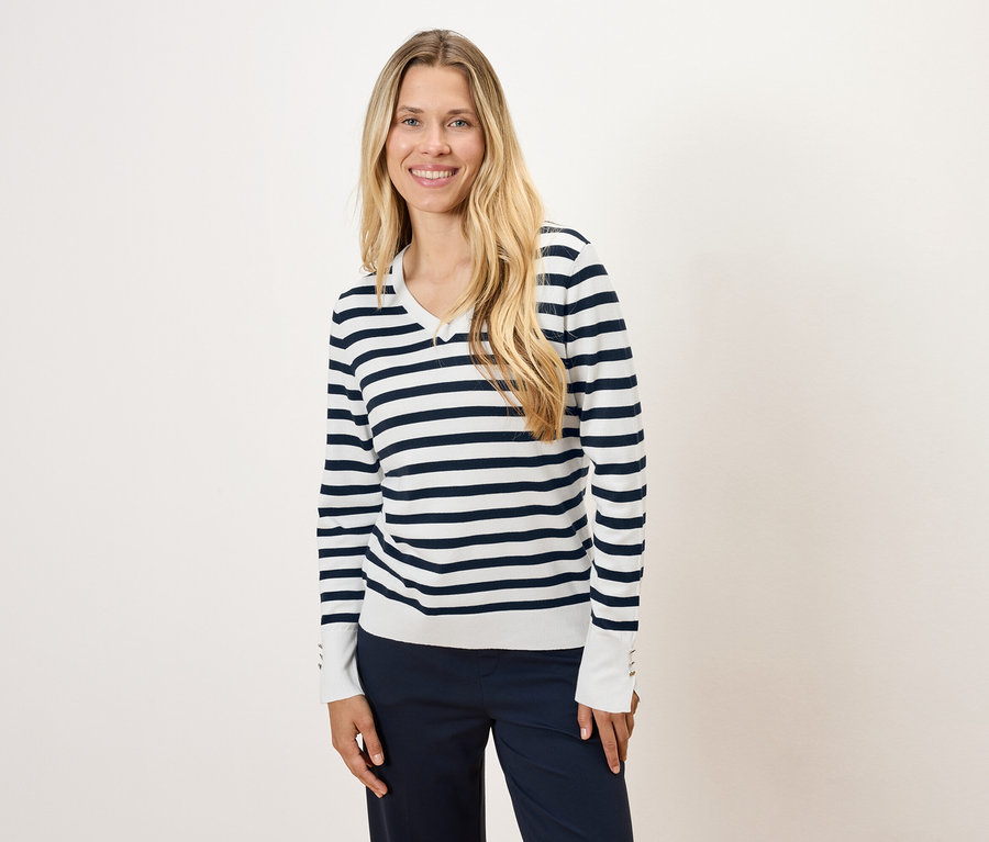 Uzun sarı saçlı bir kadın, çizgili bir kazak ve lacivert pantolon giyiyor.