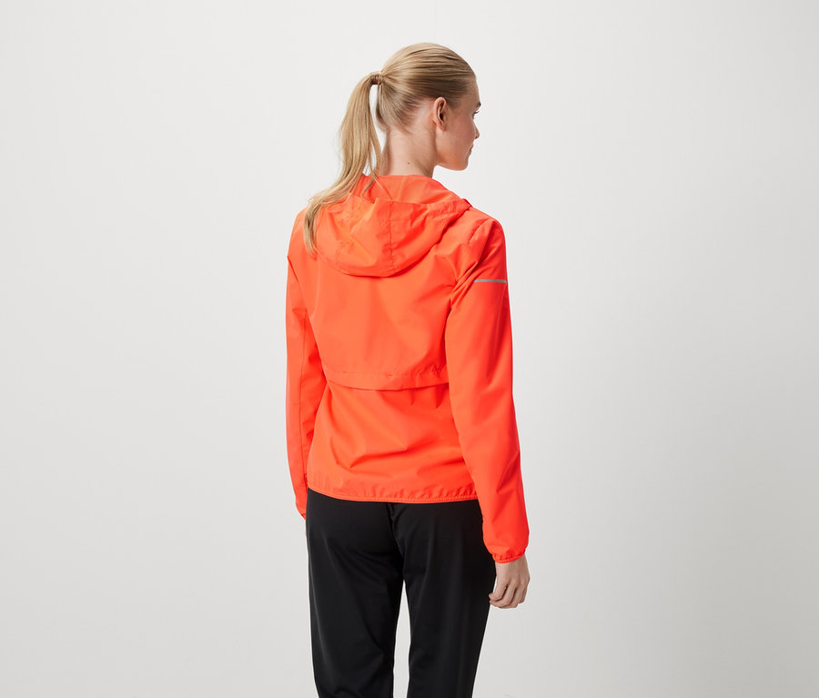 Atkuyruğu yapılmış sarı saçlı bir kadın turuncu bir ceket ve siyah pantolon giyiyor.