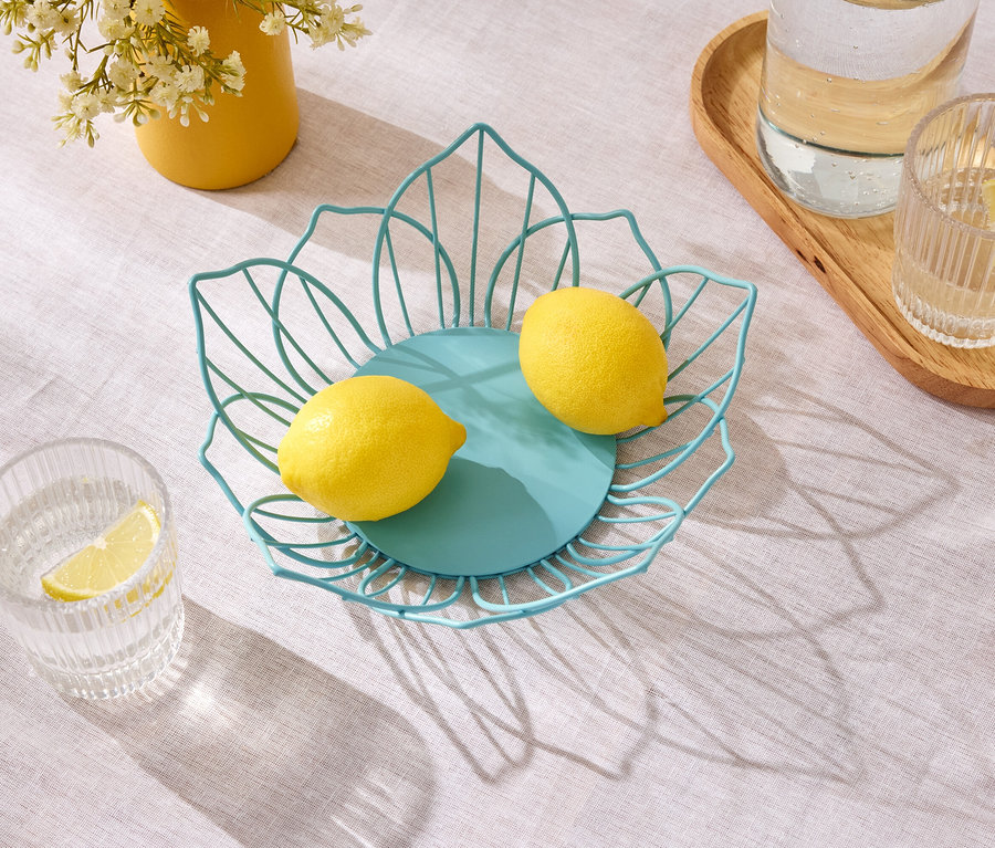 Sarı çiçekli sarı bir vazo ve su bardaklarının yanında bir masanın üzerinde mavi bir tel kabın içinde iki limon duruyor.