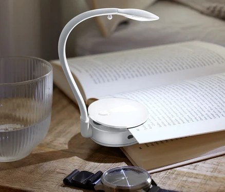 Komodinin üzerinde açık bir kitap, LED Okuma Lambası, bir bardak su ve bir kol saati duruyor.