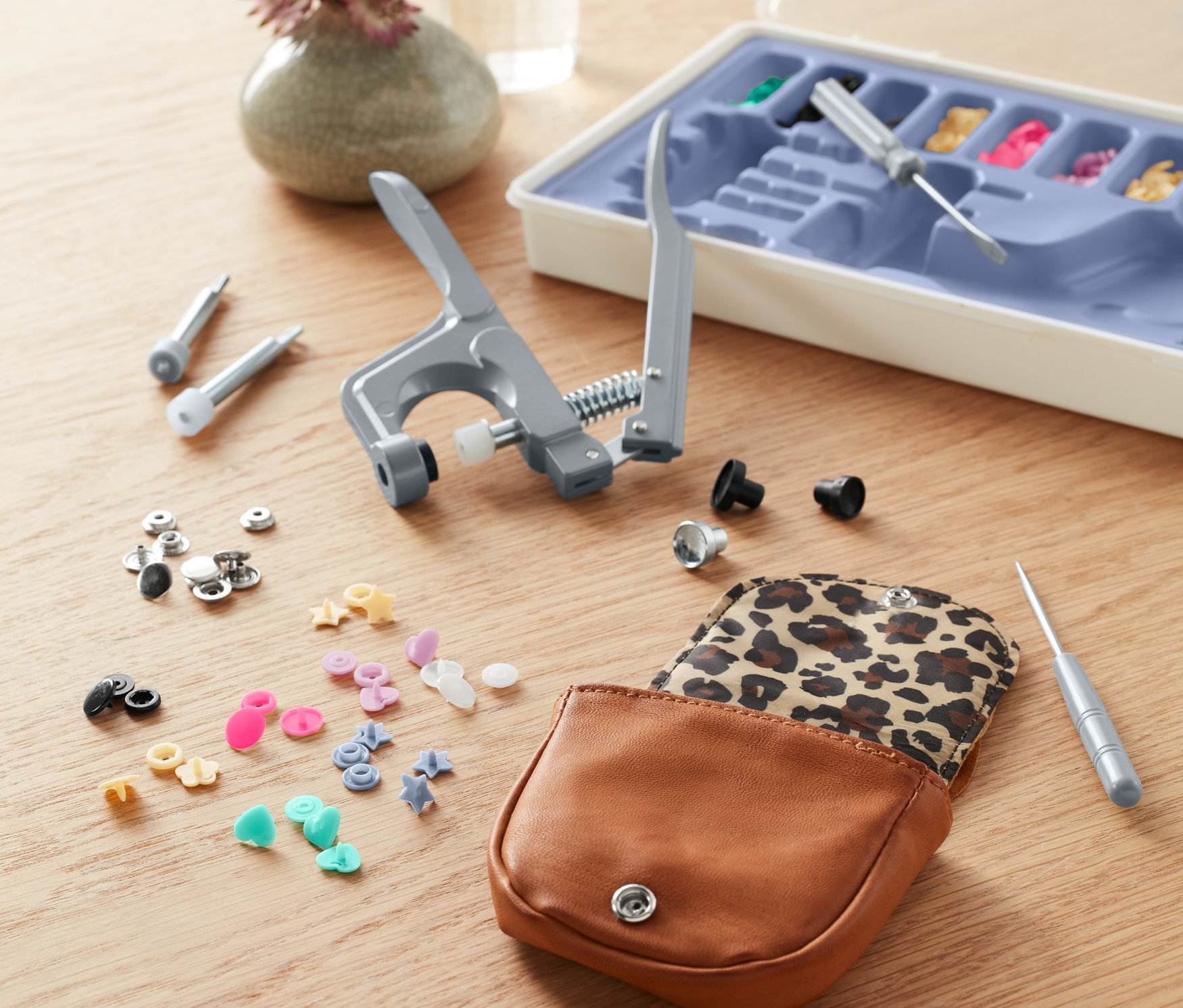 Masanın üzerinde bir çıtçıt seti, pense, aletler ve farklı çıtçıt türleri içeren açık bir kutu bulunmaktadır.