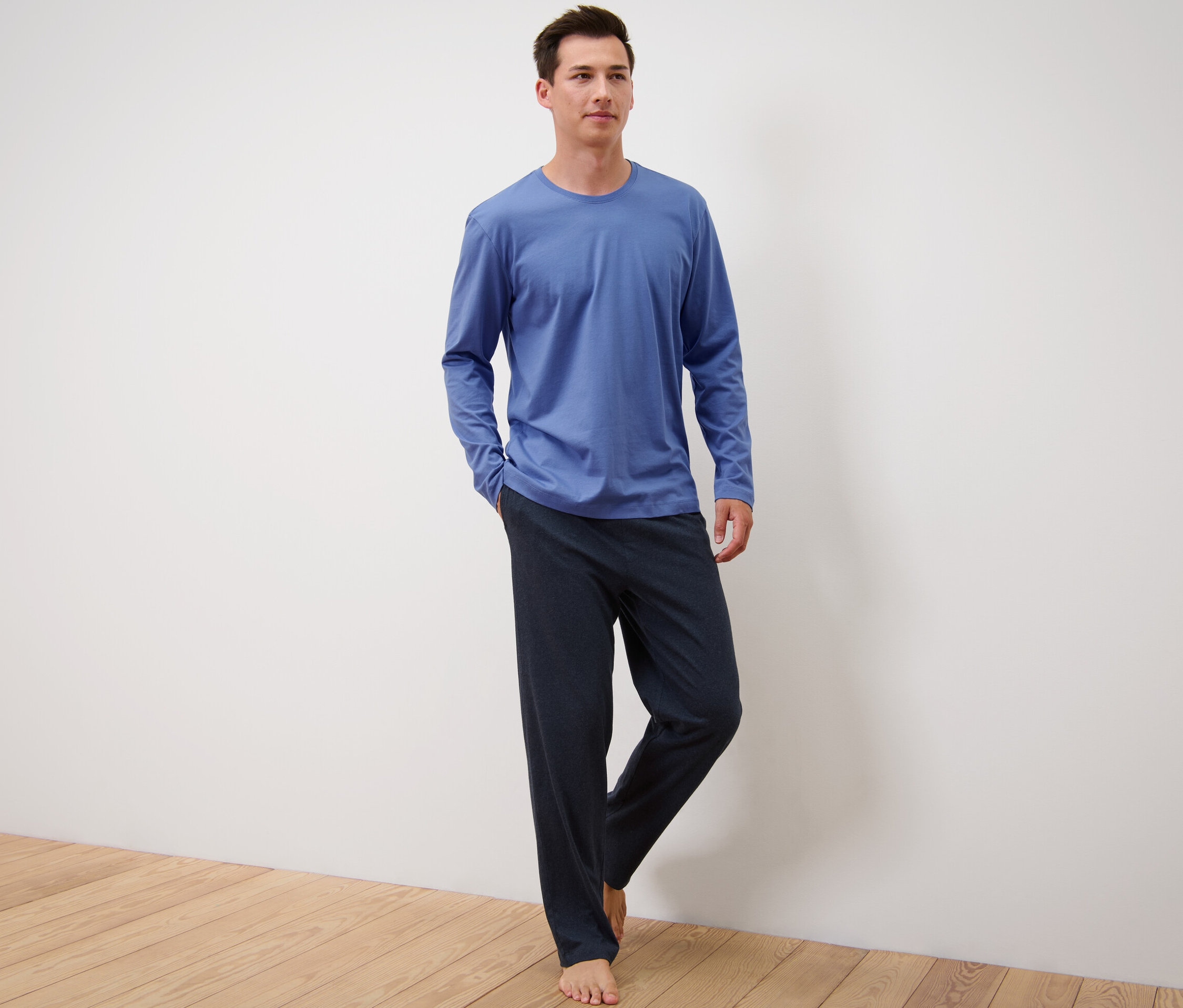 Ayakta duran bir adam mavi-lacivert pijama takımı giyiyor.