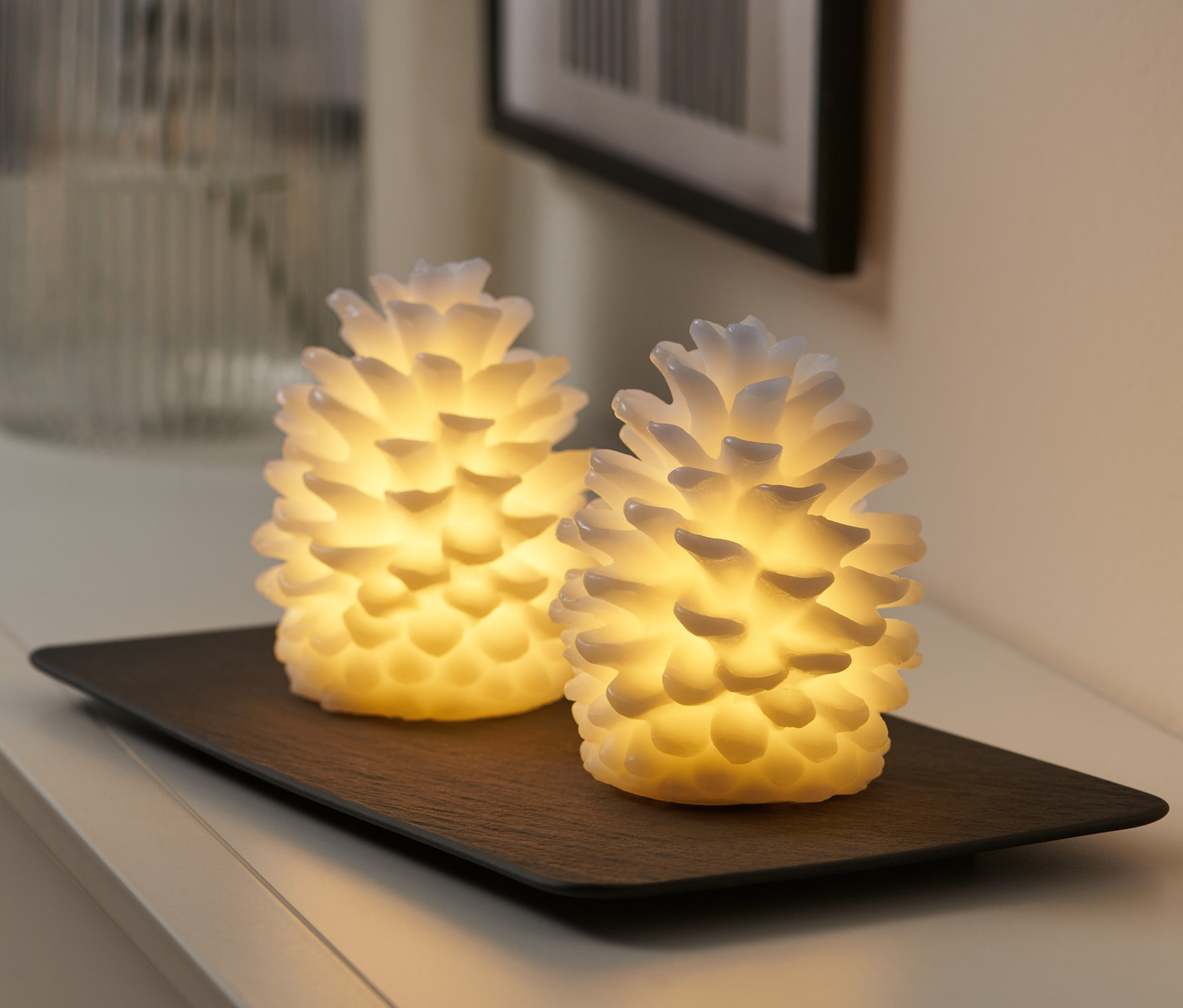 Siyah bir tepside duran 2 adet LED çam kozalağı mum.