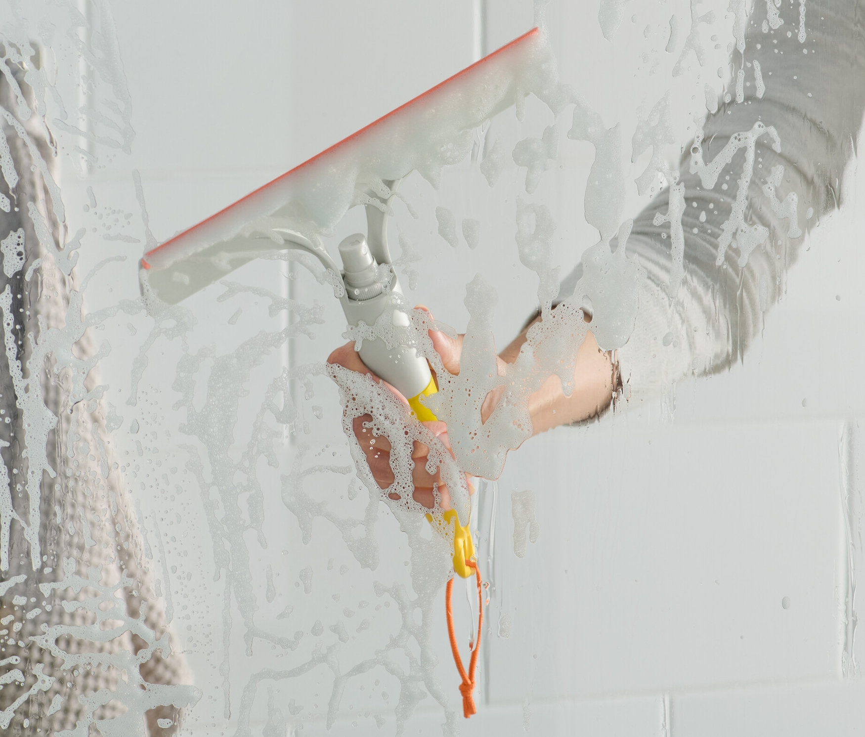 Kadın, 3'ü 1 arada cam silici ile cam duşakabini siliyor.