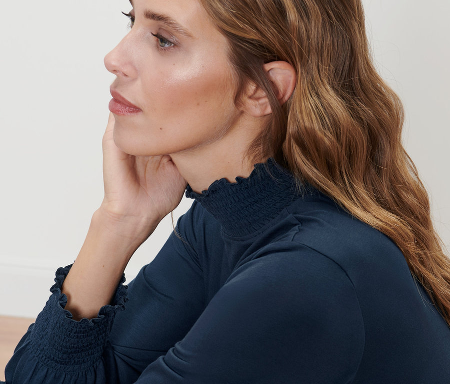 Kahverengi saçlı, dik yakalı koyu mavi bluz giyen bir kadının profili.