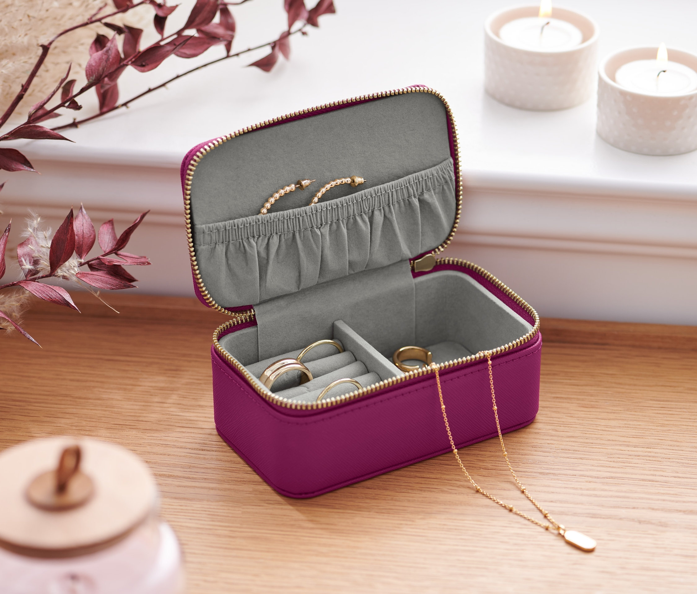 Ahşap bir masa üzerinde altın fermuarlı, mor renkli, açık küçük bir takı kutusu. İçinde yüzükler, bir kolye ve bir bilezik var.