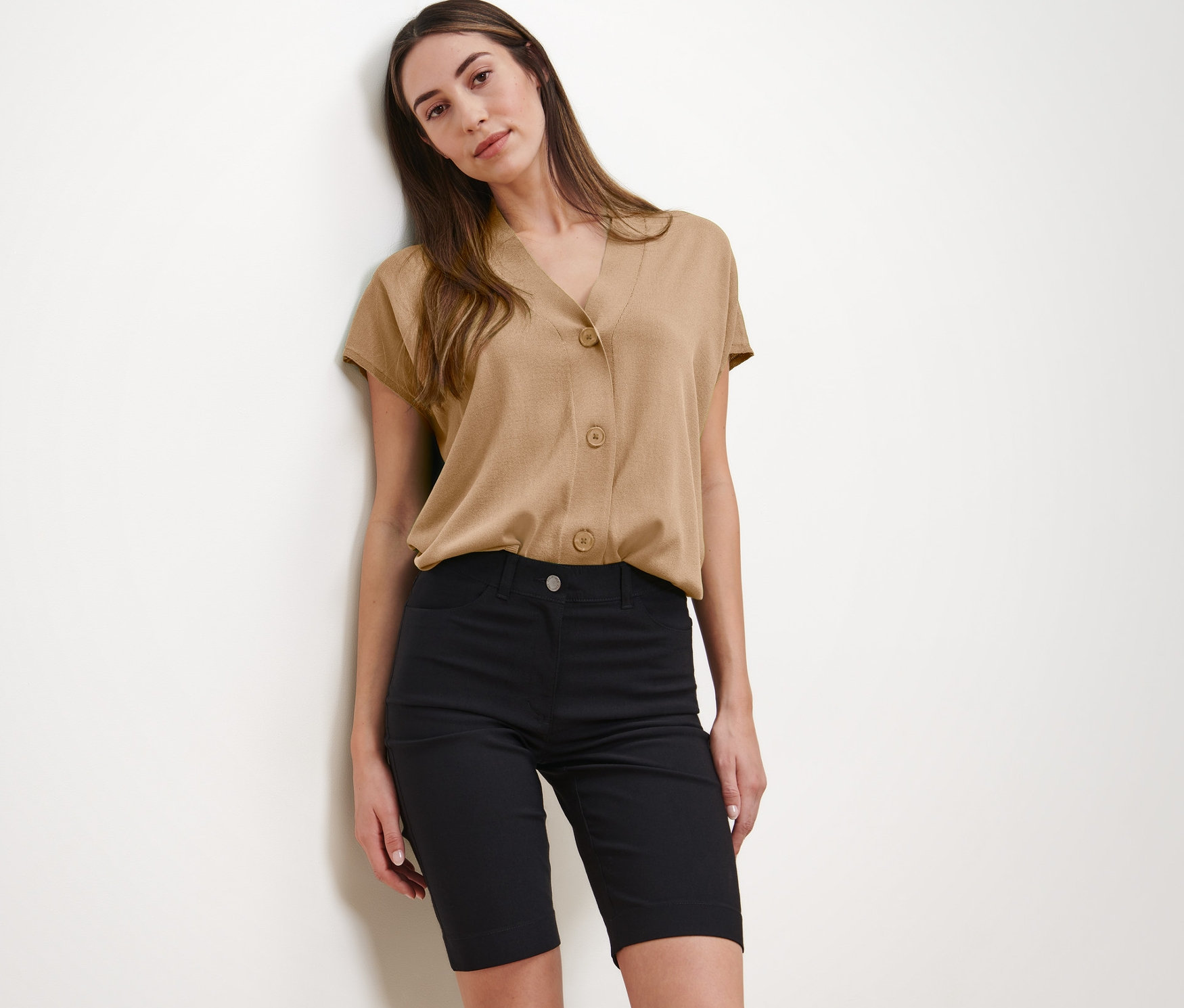 Kadın bej bluz ve siyah Bengalin Bermuda Şort ile poz veriyor.