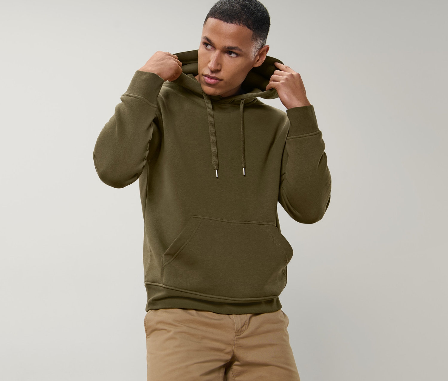 Zeytin yeşili kapüşonlu bir ürünün kapüşonunu ayarlayan adam. Bej şort giyiyor.