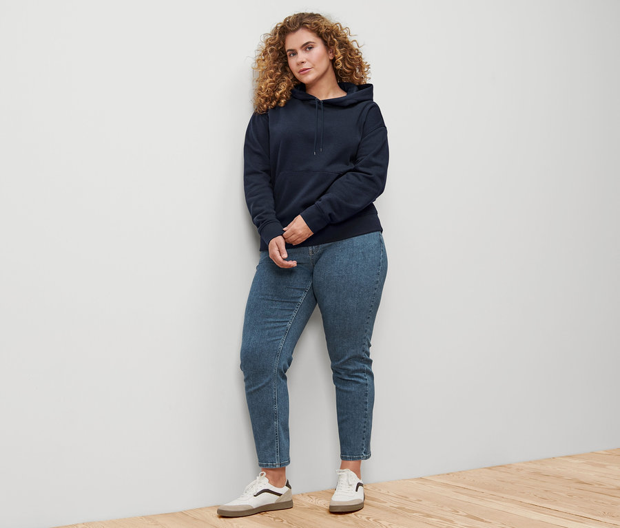 Duvara yaslanmış koyu lacivert kapüşonlu sweatshirt giyen bir kadın.