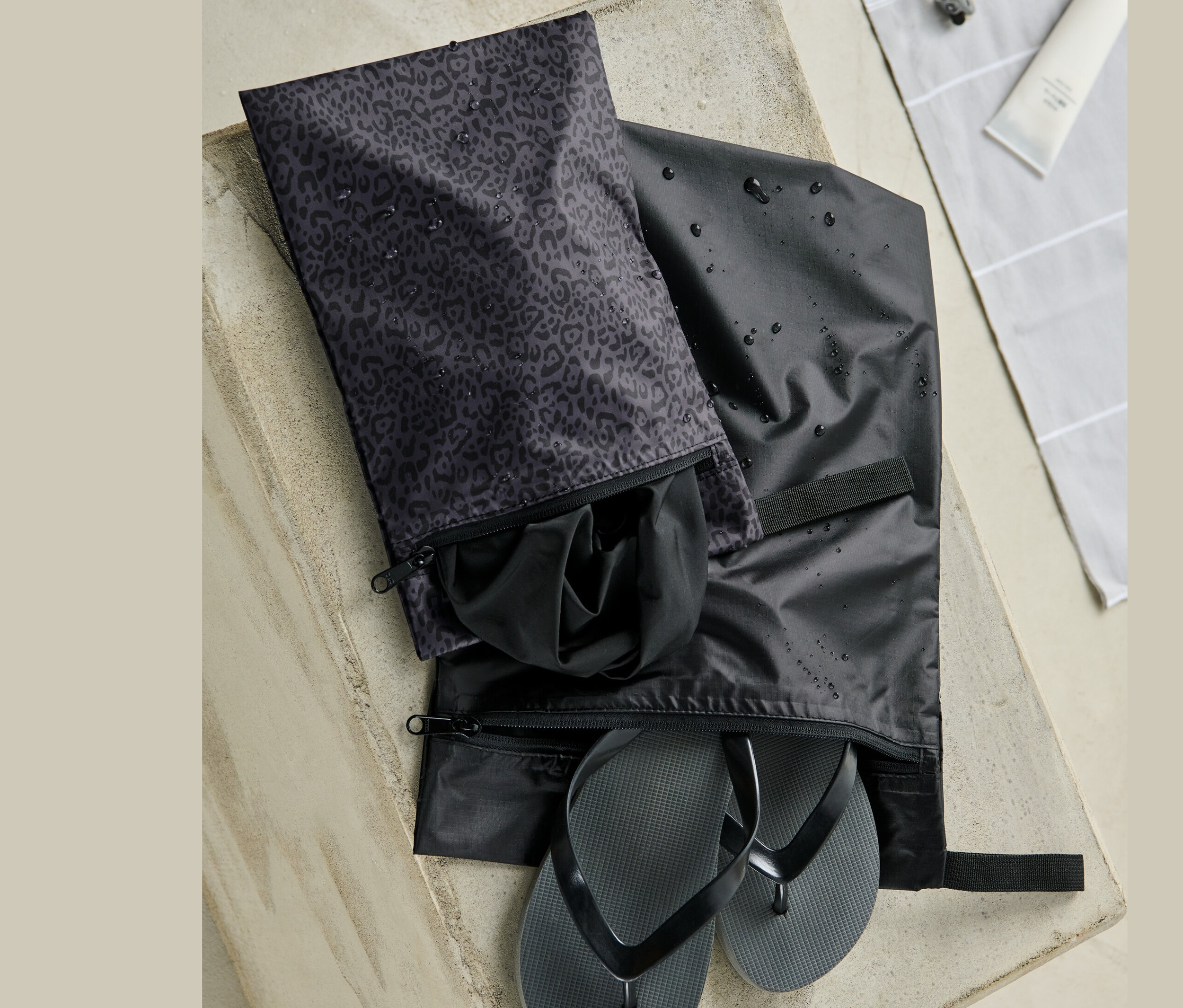 Beton yüzey üzerinde iki adet su geçirmez torba. Birinde siyah parmak arası terlikler, diğerinde siyah giysiler var.